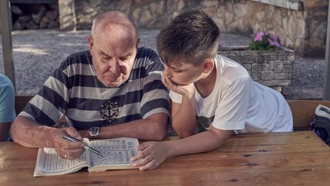 Großvater erklärt seinem Enkel ein Kreuzworträtsel. (Foto: IMAGO, IMAGO/ Cavan Images)