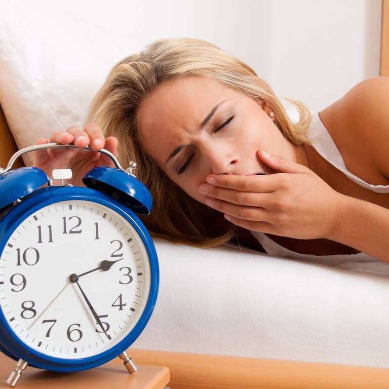  Blonde Frau liegt im Bett und kann nicht schlafen. Sie gähnt, ihr Wecker zeigt 2.25 Uhr in der Nacht (Foto: IMAGO, /McPHOTO)