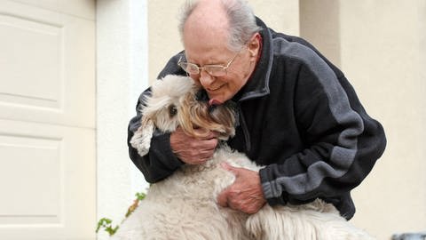 älterer Herr schmust mit seinem Hund (Foto: IMAGO, Design Pics)