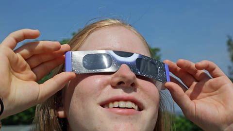 Das Foto zeigt ein Kind, das mit einem speziellen Augenschutz eine Sonnenfinsternis beobachtet. (Foto: IMAGO, Eibner)
