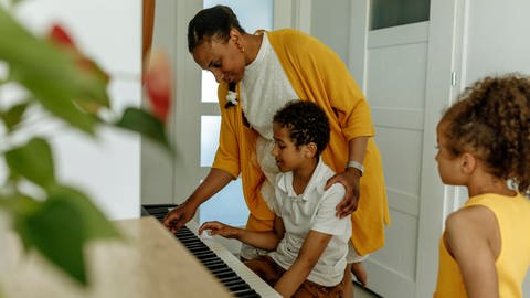 Eine Mutter bringt ihren Kindern das Klavierspielen bei. (Foto: IMAGO, IMAGO / Westend61)