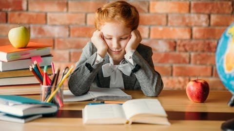 Das Bild zeigt eine Schülerin, die müde über ihren Hausaufgaben sitzt. (Foto: IMAGO, Panthermedia)
