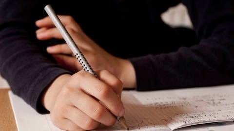 Grundschüler schreibt mit einem Bleistift ins Heft (Foto: IMAGO, /blickwinkel)