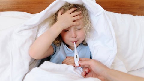 Das Bild zeigt ein krankes Kind, das mit Fieber im Bett liegt. (Foto: IMAGO, Westend61)