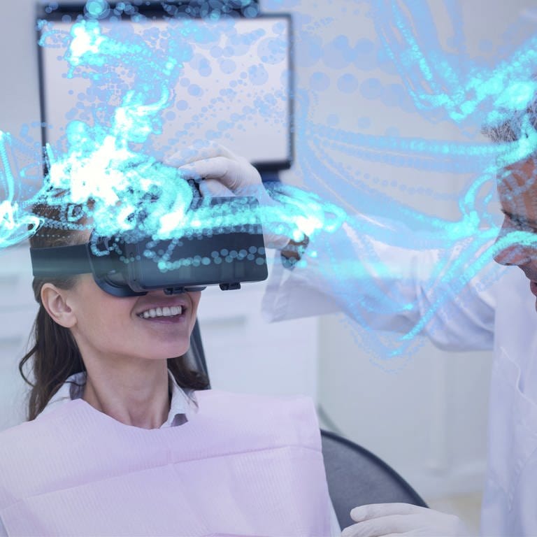 Eine Frau auf einer Behandlungsliege trägt eine VR-Brille und lacht, während ein Mann den Sitz der VR-Brille bei ihr überprüft. (Foto: IMAGO, -)
