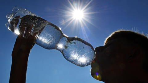 Ein Mann trinkt bei strahlender Sonne aus einer Wasserflasche. (Foto: IMAGO, IMAGO / Sven Simon)