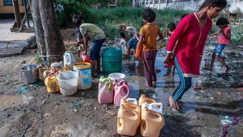 Slumkinder aus Indien sammeln Trinkwasser und Wasser für den täglichen Gebrauch aus einem Leck in einer Wasserleitung am Straßenrand.  (Foto: IMAGO, /ZUMA Wire)