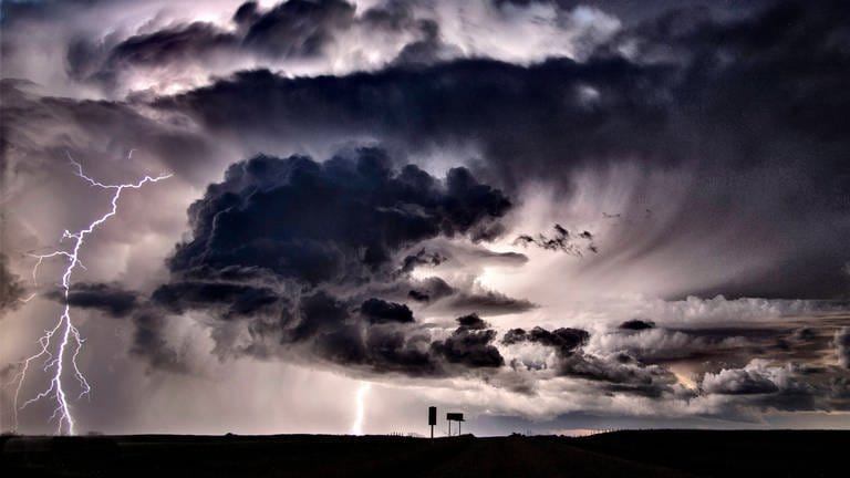 Ein Blitz schlägt aus einer dunklen Gewitterwolke auf die Erdoberfläche ein. (Foto: IMAGO, IMAGO / Zoonar)