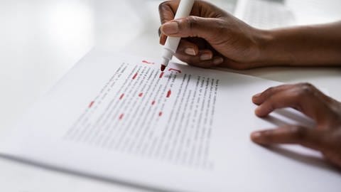 Eine Frau markiert Korrekturen in einem Text mit einem roten Stift.