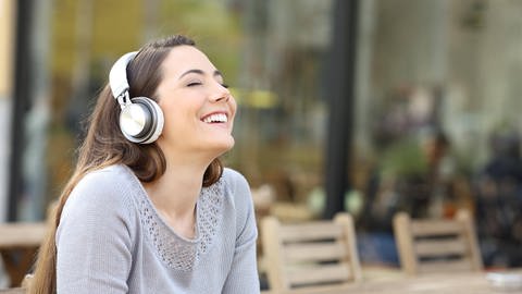 Frau lächelt und hat Kopfhörer auf. Zu laute Musik kann die Ohren stark belasten. (Foto: IMAGO, /Panthermedia)