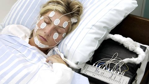 Frau mit Elektroden am Kopf und Gesicht im Schlaflabor (Foto: IMAGO, / photo2000)
