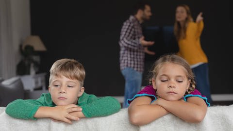Kinder lehnen über dem Sofa während sich die Eltern im Hintergrund streiten (Foto: IMAGO, /Panthermedia)