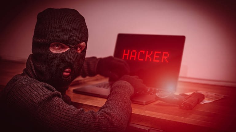 Das Bild zeigt einen Mann mit Skimaske vor einem Rechner. Auf dem Bildschirm steht "Hacker". (Foto: IMAGO, Bihlmayerfotografie)