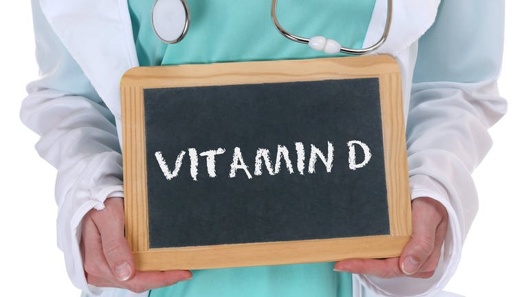 Arzt hält ein Schild mit der Aufschrift "Vitamin D" hoch. Generell sollte Vitamin D nur mit Absprache eines Arztes oder einer Ärztin zu sich genommen werden. (Foto: IMAGO, /Aviation-Stock)