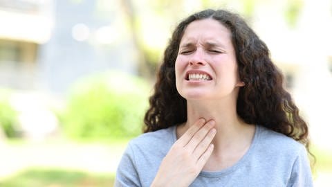 Eine Frau mit schmerzverzerttem Gesicht fasst sich an den Hals. (Foto: IMAGO, IMAGO / Panthermedia)