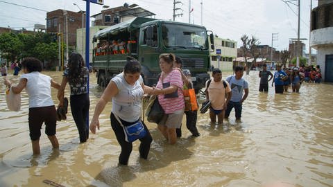 Eine Gruppe von Menschen versuchen eine überflutete Straße in Peru zu überqueren.
