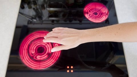 Eine Hand fühlt über einer angeschalteten Herdplatte. (Foto: IMAGO, IMAGO / imagebroker)