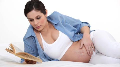 Eine schwangere Frau liest ein Buch auf dem Bett. (Foto: IMAGO, IMAGO / Panthermedia)