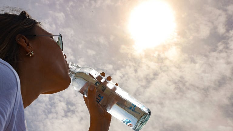 Eine Frau trinkt Wasser an einem sonnigen Tag. (Foto: IMAGO, IMAGO / localpic)