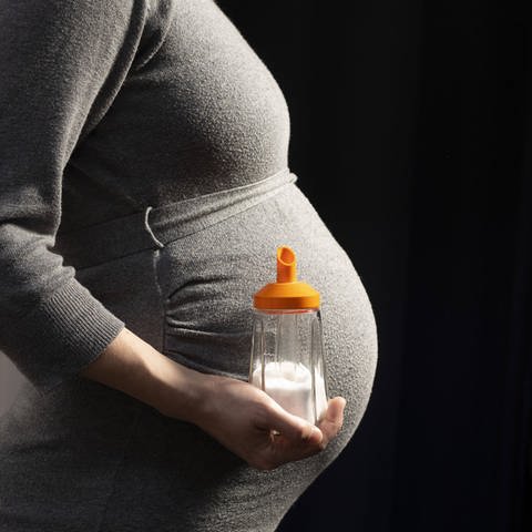 Eine schwangere Frau hält einen Zuckerstreuer vor ihren Babybauch.