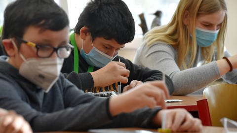 Das Bild zeigt Schülerinnen und Schüler mit Schutzmasken, die in einem Klassenraum Corona-Tests durchführen.