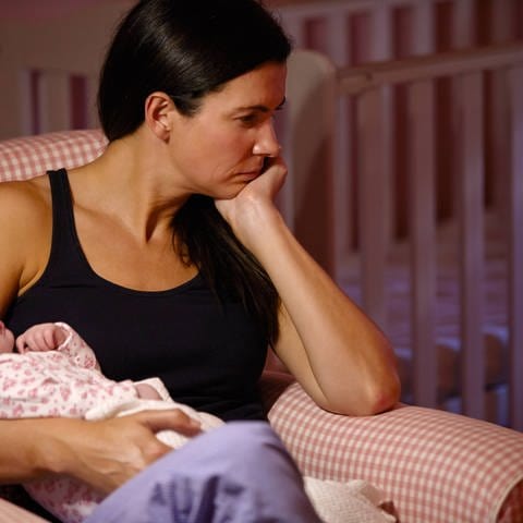 Das Bild zeigt eine Mutter, die traurig in die Ferne guckt, als sie ihr Kind hält.