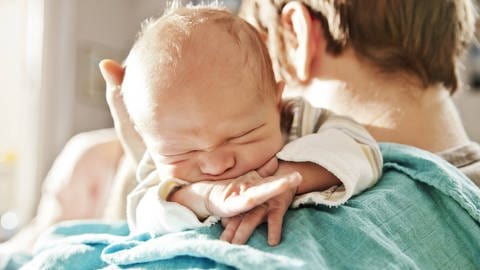 Das Bild zeigt ein Baby, das mit dem Kopf auf der Schulter des Vaters liegt.