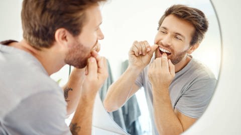 Das Bild zeigt einen Mann, der Zahnseide verwendet