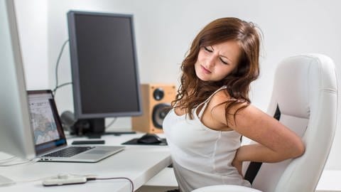 Das Bild zeigt eine Frau am Schreibtisch, die sich schmerzverzerrt den Rücken hält. (Foto: IMAGO, Panthermedia)