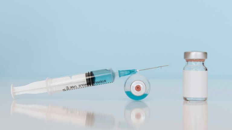 Das Bild zeigt eine Spritze und zwei Impf-Ampullen.