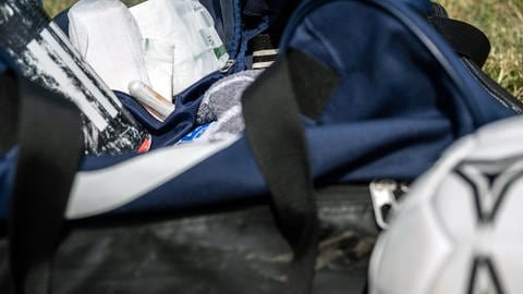 Sporttasche liegt auf Wiese. Darin sind Tampons und Binden, davor liegt ein Fußball. (Foto: picture-alliance / Reportdienste, picture alliance/dpa | Pia Bayer)