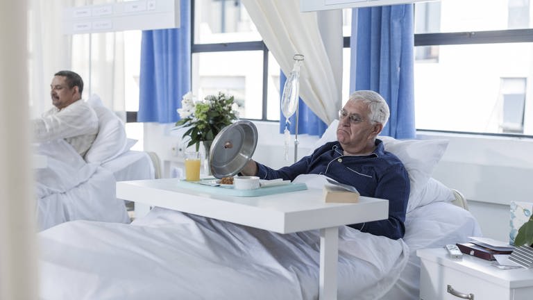 Das Bild zeigt einen älteren Herrn im Krankenhaus mit Krankenhausessen. Symbolbild. (Foto: IMAGO, Westend61)