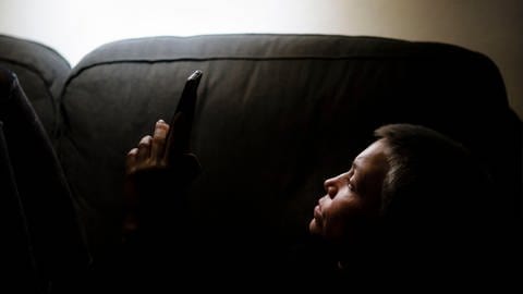 Social Media kann besonders bei jungen Menschen anfängliche Symptome psychischer Erkrankungen verstärken. | Eine Frau sitzt nachts alleine auf der Coach und schaut in ein Smartphone. (Foto: picture-alliance / Reportdienste, picture alliance / photothek | photothek/ Thomas Trutschel)