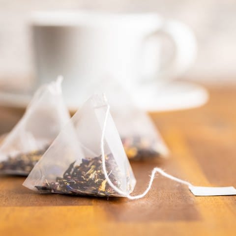 Teebeutel liegen vor einer Teetasse: Seit Jahren wird Tee verstärkt in pyramidenförmigen Kunststoffbeuteln angeboten. Teebeutel wie früher aus einfacher Zellulose, also Papierfasern, werden weniger. 