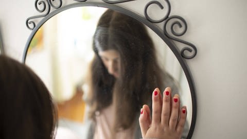 Vorsätze für das neue Jahr sind häufig nicht realistisch formuliert. Eine junge Frau senkt enttäuscht den Blick vor einem Spiegel.