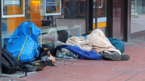 Eine obdachlose Person schläft bei eisiger Kälte auf dem Boden.