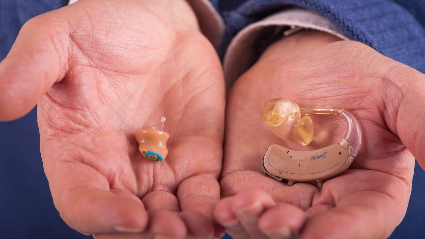 Zwei Hörgeräte liegen in den Händen eines älteren Mannes (Foto: IMAGO, Depositphotos)
