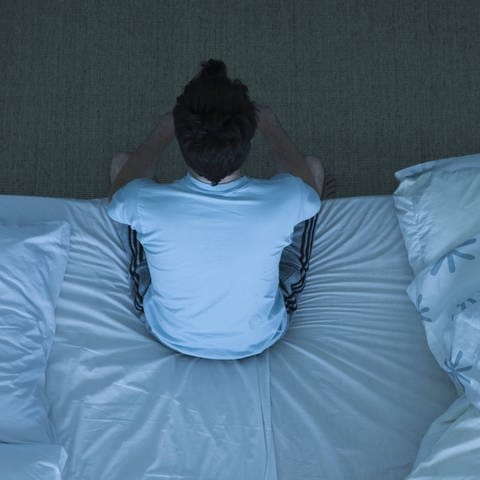 Mann sitzt auf Bettkante, unfähig zu schlafen, tags: weißes, pinkes, braunes Rauschen (Foto: IMAGO, https://www.imago-images.de/st/0085384325)
