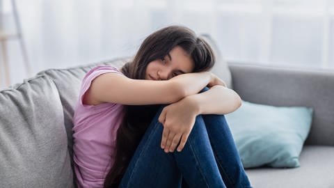 Mädchen sitzt deprimiert auf dem Sofa, tags: Schulschließungen, Pandemie, Homeschooling