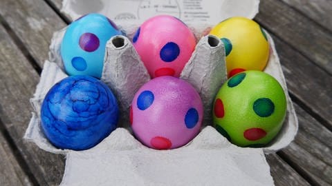 Bunte Eier aus dem Supermarkt sollten gekühlt gelagert werden.  Das Bild zeigt bemalte Ostereier in einem Eierkarton. Symbolbild. (Foto: IMAGO, CHROMORANGE)