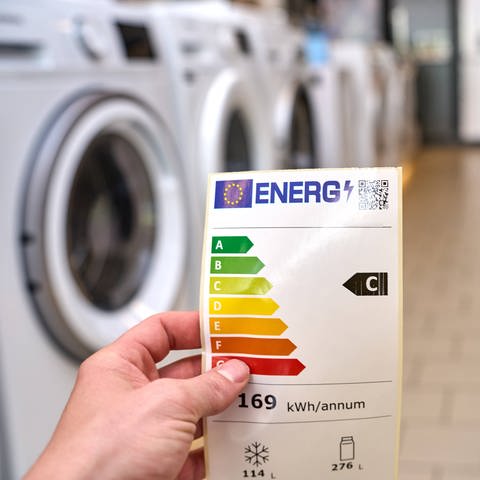 Energieeffizienz-Label vor einem Gang von Waschmaschinen. 