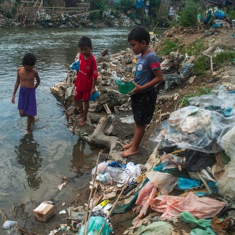 Indonesische Kinder spielen am zugemüllten Fluss.
