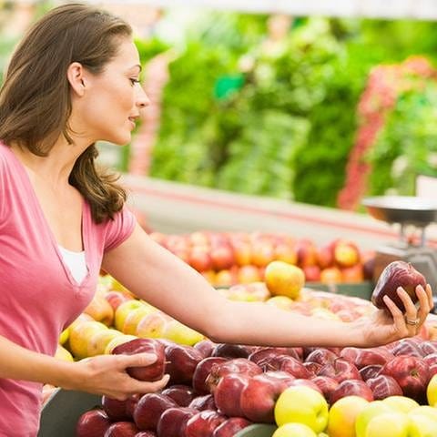 Eine Frau beim Einkaufen, sie hält einen roten Apfel in der Hand und begutachtet ihn.