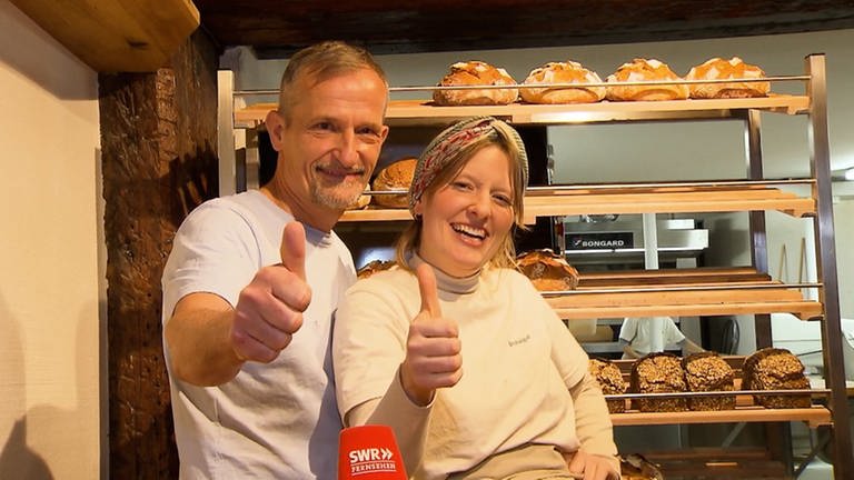Hausarzt Jörn und seine Tochter Nora stehen lachend vor der Auslage, in der frische Brote liegen, in ihrer Konstanzer Bäckerei. Sie machen beide einen Daumen nach oben.  (Foto: SWR)