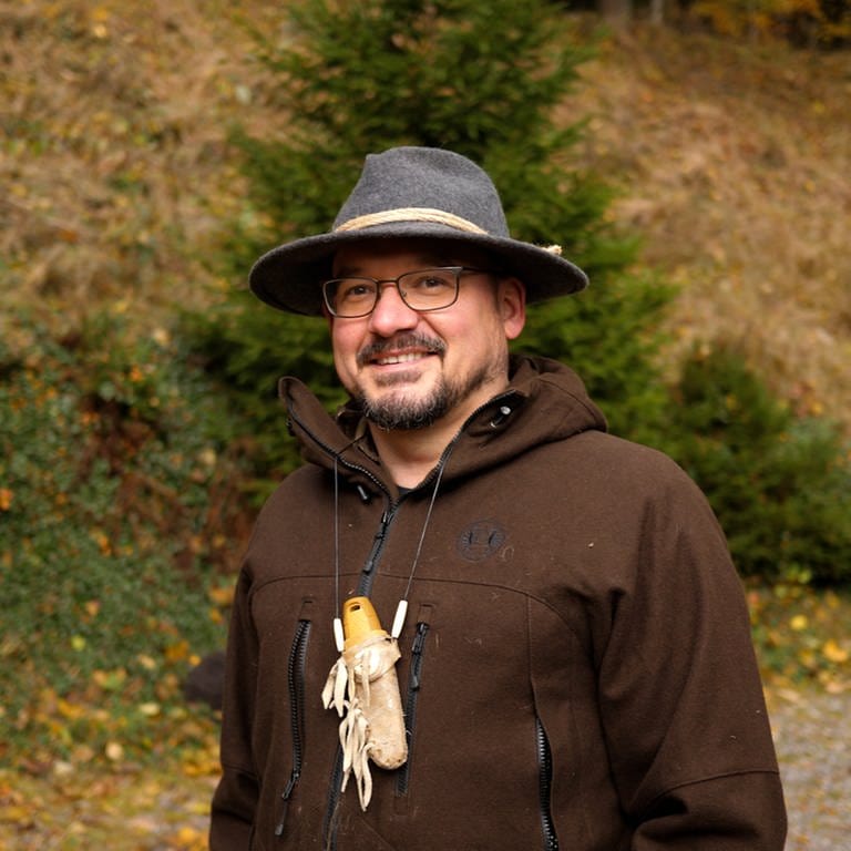 Der Survival Profi Ralf lächelt in die Kamera. Er steht mitten im Wald, sein Revier.  (Foto: SWR)