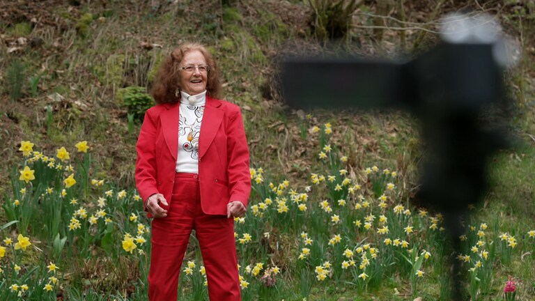 Thea rockt - ältere Frau in rotem Kostüm vor blühender Hecke (Foto: SWR)