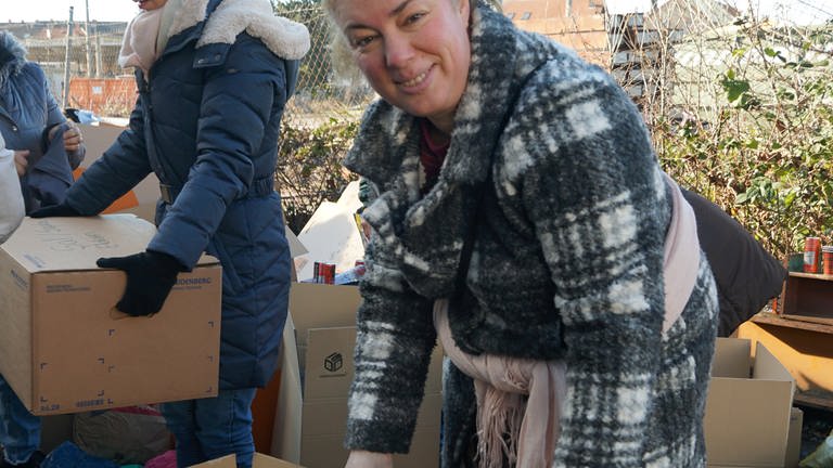Ältere Frau in einer grau-weißen Jacke packt zwei Kartons mit Kleidung.  (Foto: SWR)