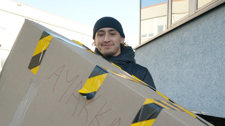Junger Mann, mit Mütze trägt einen riesigen Karton.  (Foto: SWR)