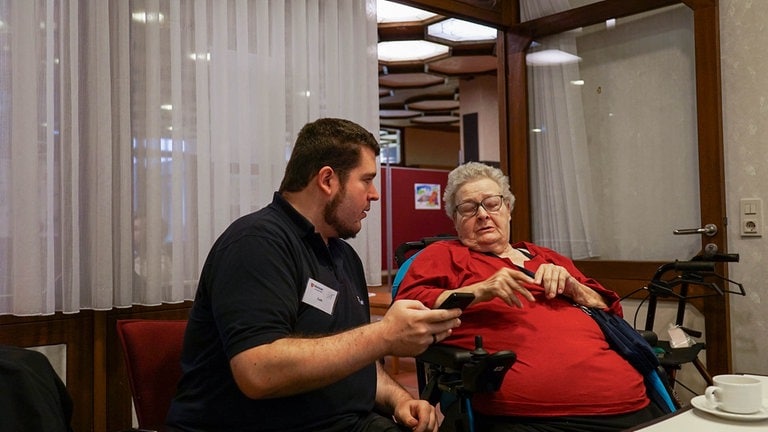 Ein Mitarbeiter vom IT-Café sitzt neben Ursula und klärt sie über Fahren im Internet auf. (Foto: SWR) Ein Mitarbeiter vom IT-Café sitzt neben Ursula und klärt sie über Fahren im Internet auf.