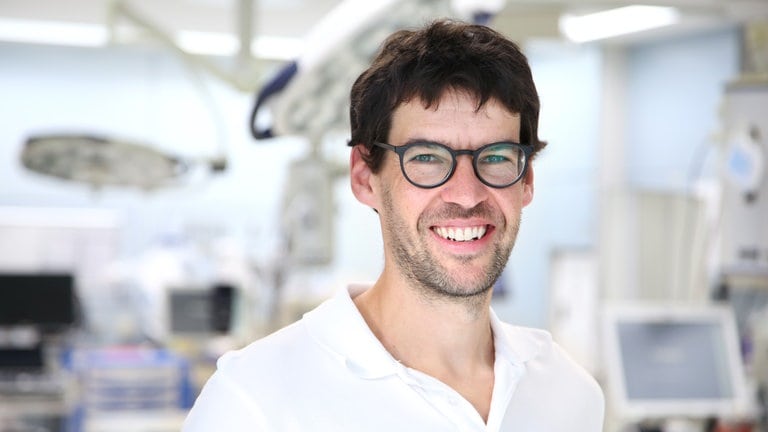 Axel ist in seinem sechsten Weiterbildungsjahr zum Facharzt für Orthopädie und Unfallchirurgie. Er steht im OP und lächelt in die Kamera (Foto: SWR) Axel ist in seinem sechsten Weiterbildungsjahr zum Facharzt für Orthopädie und Unfallchirurgie. Er steht im OP und lächelt in die Kamera